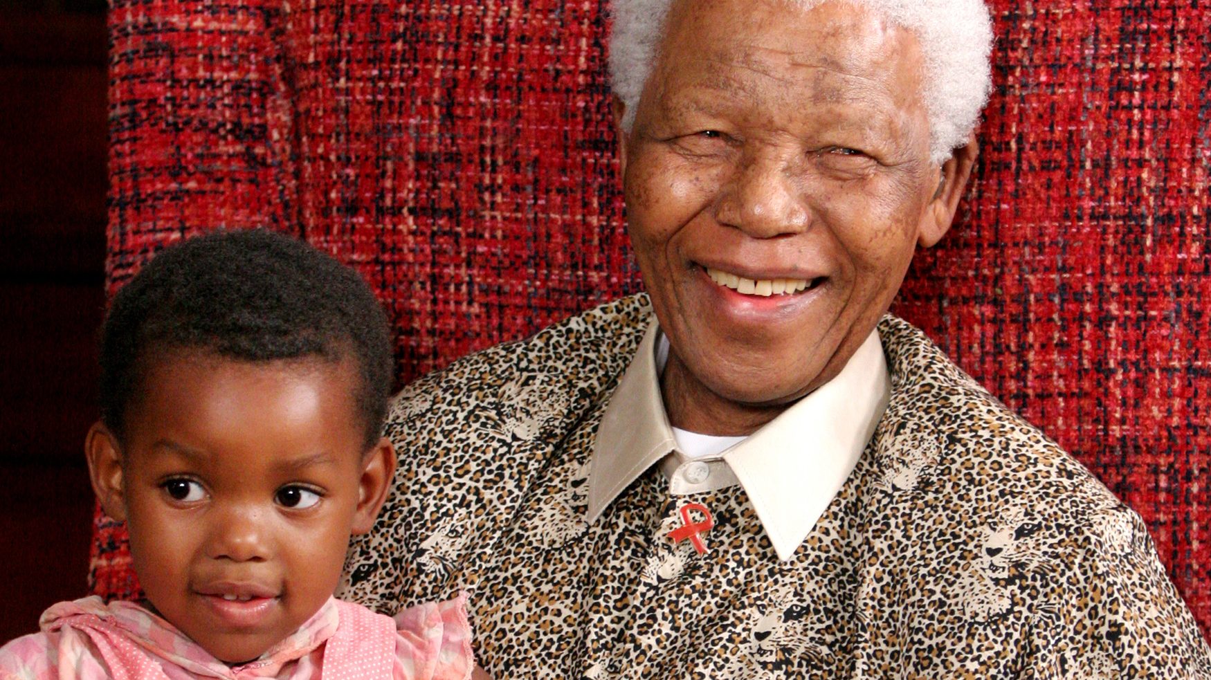 Nelson Mandela lacht naar de camera en heeft een kind op zijn schoot. 